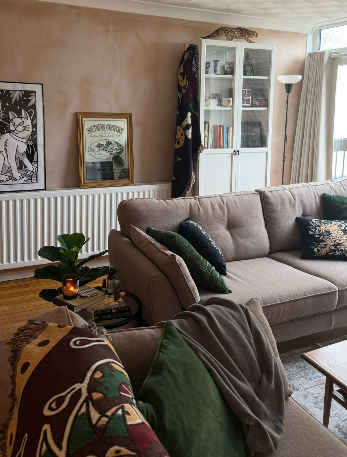 A cozy living room scene featuring a taupe fabric sectional sofa with dark green and patterned accent pillows, a textured scalloped ceiling, and a white glass cabinet in the background.